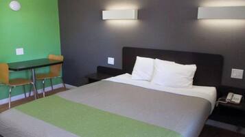 A hotel room with a bed, a desk, two chairs, and a green wall.