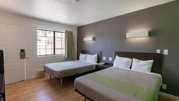 A hotel room with two single beds, a window with curtains, a door, and a light switch on the wall.