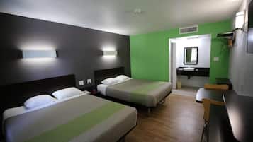 A hotel room with two beds, a bathroom with a mirror and sink, and a small table.