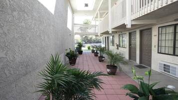 A corridor with potted plants, a tiled floor, and a building with a balcony on the right.
