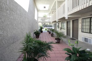 A corridor with potted plants, a tiled floor, and a building with a balcony on the right. - 2 Queen Beds | Non-Smoking, Kitchen (Barstow)