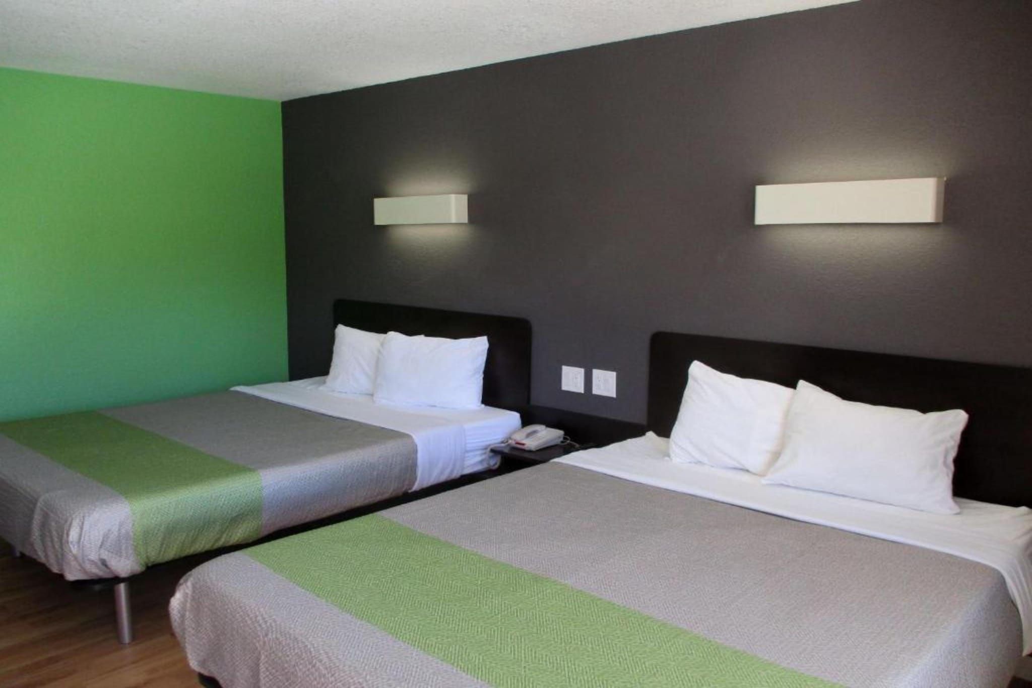 A hotel room with two beds, each with white linens and a green and gray striped blanket. There are two wall-mounted lights above each bed.