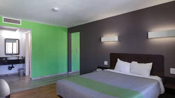 A hotel room with a bed, a nightstand, a mirror, and a bathroom with a sink.
