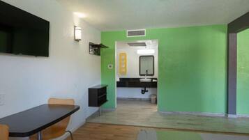 A room with a dining table, chairs, a TV mounted on the wall, and a bathroom with a mirror and sink.