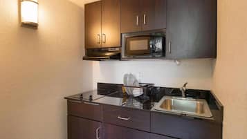 A compact kitchenette with dark cabinetry, a stainless steel sink, a microwave, and a gas stove.