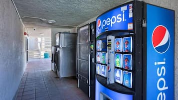 A vending machine with a Pepsi logo, a refrigerator, and a trash can in a corridor.
