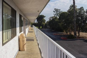 A covered outdoor area with a wooden deck, a trash can, and a view of a parking lot with trees.