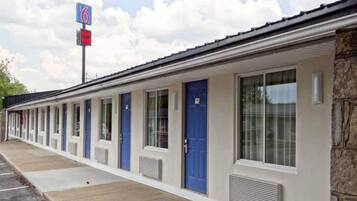 A motel with a row of rooms, each with a blue door and a window. There is a sign indicating the motel number.
