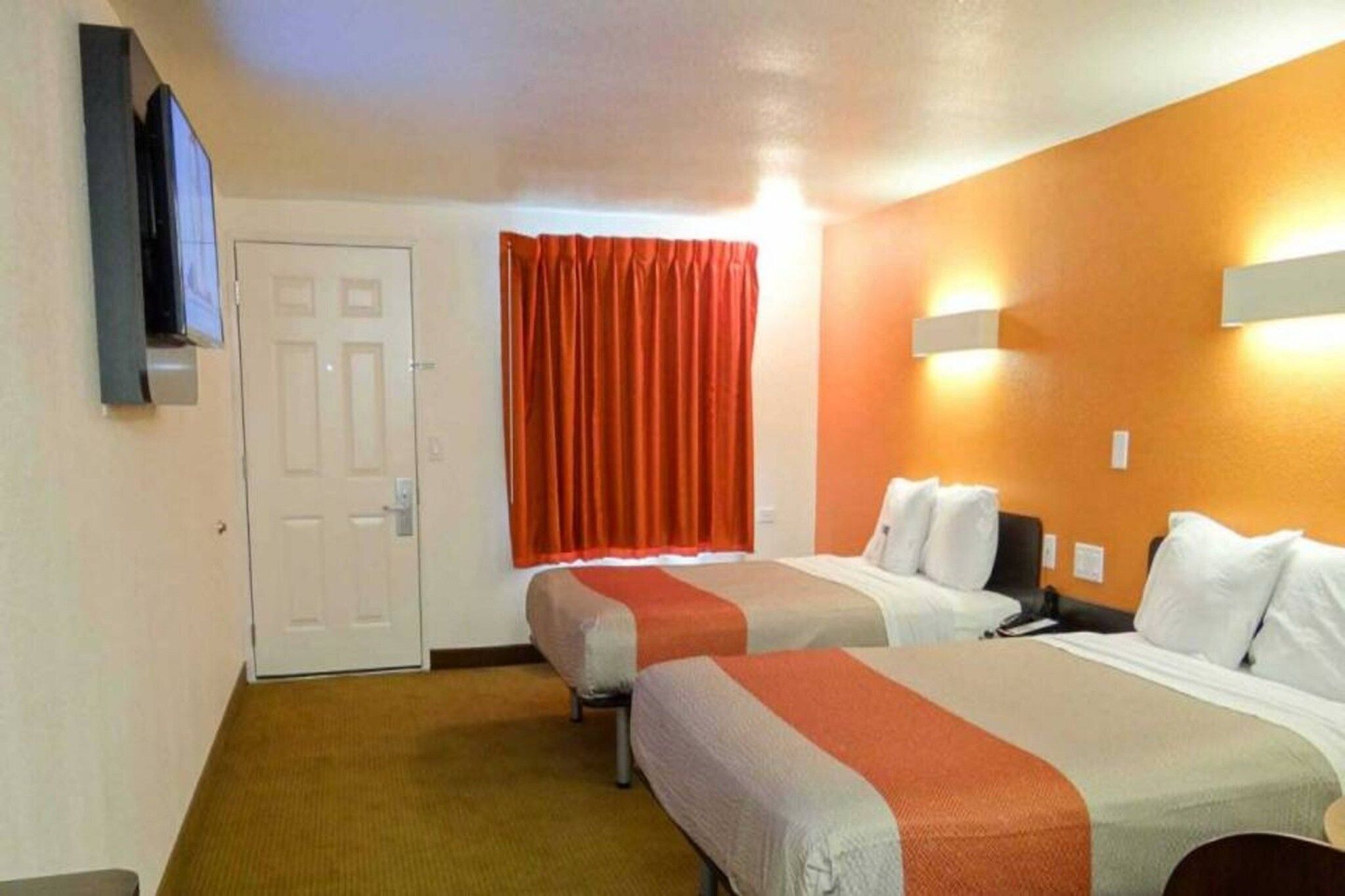 A hotel room with two beds, a television, a door, and a window with curtains.