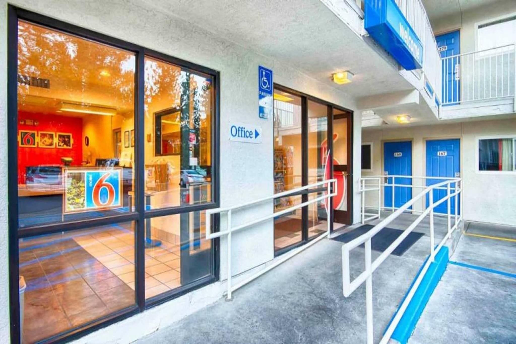 A hotel entrance with a reception area, an office sign, and a blue wheelchair-accessible ramp.