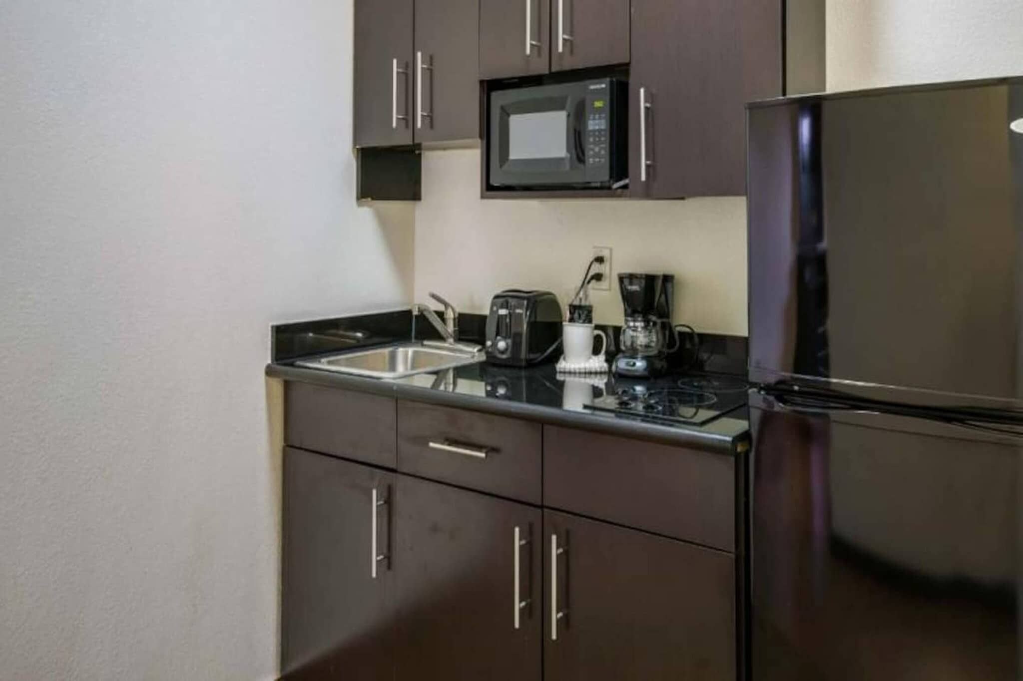 A compact kitchen with a microwave, toaster, coffee maker, and refrigerator.