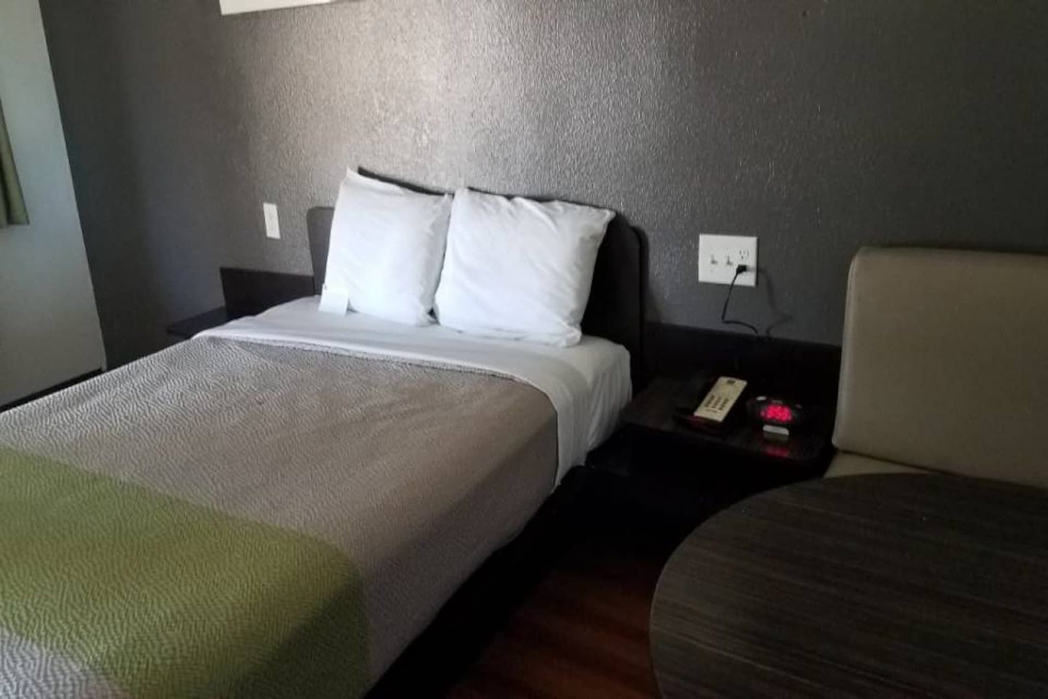 A hotel room with a bed, a bedside table with a phone, and a chair.