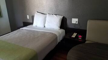 A hotel room with a bed, a bedside table with a phone, and a chair.