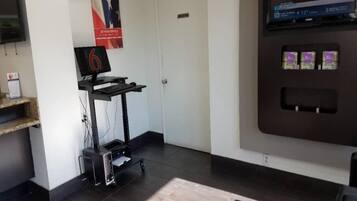 A reception area with a desk, a computer, a printer, a wall-mounted TV, and a vending machine.