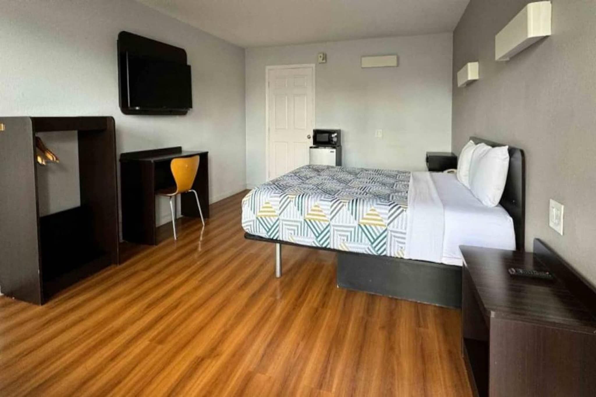 A hotel room with a bed, a desk, a chair, a television, and a door.