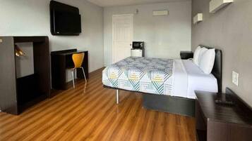 A hotel room with a bed, a desk, a chair, a television, and a door.