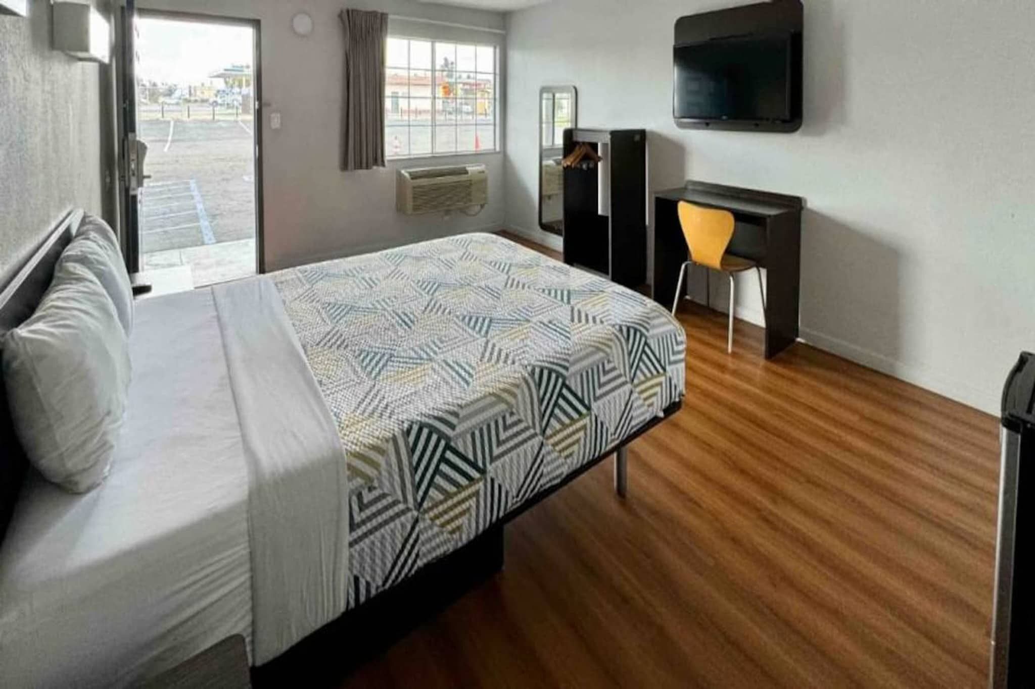 A hotel room with a bed, a desk, a chair, a TV, and a window.