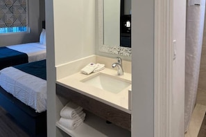 A hotel room with a bed, a bathroom with a sink and mirror, and a patterned wall. - Cozy Queen Bed|Pool|Free Parking (Williams)