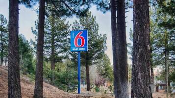 A motel sign with a number 6 and a Wi-Fi symbol, surrounded by tall pine trees.