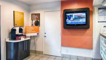 Uma área de recepção com tela digital, espaço para café e placas informativas.