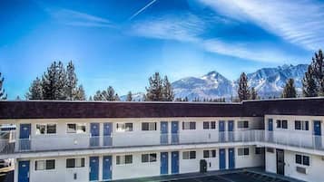 A motel with a two-story structure, a parking lot in front, and a mountain backdrop.