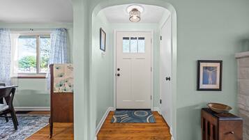 A hallway with a white door, a patterned rug, and a small table with a bowl.