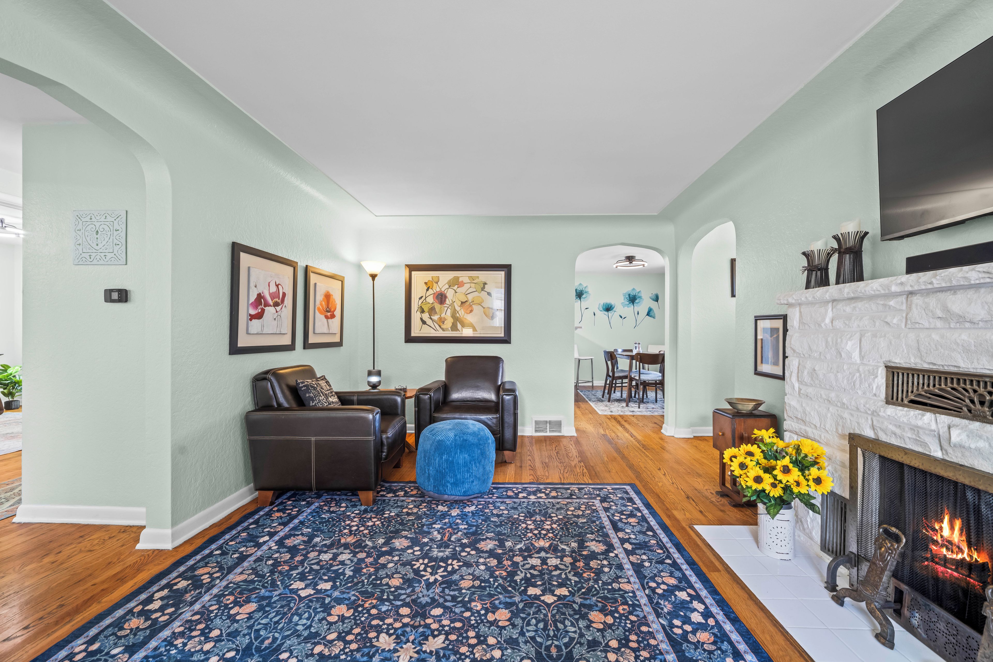 A living room with a fireplace, a blue patterned rug, and a dining area in the background.