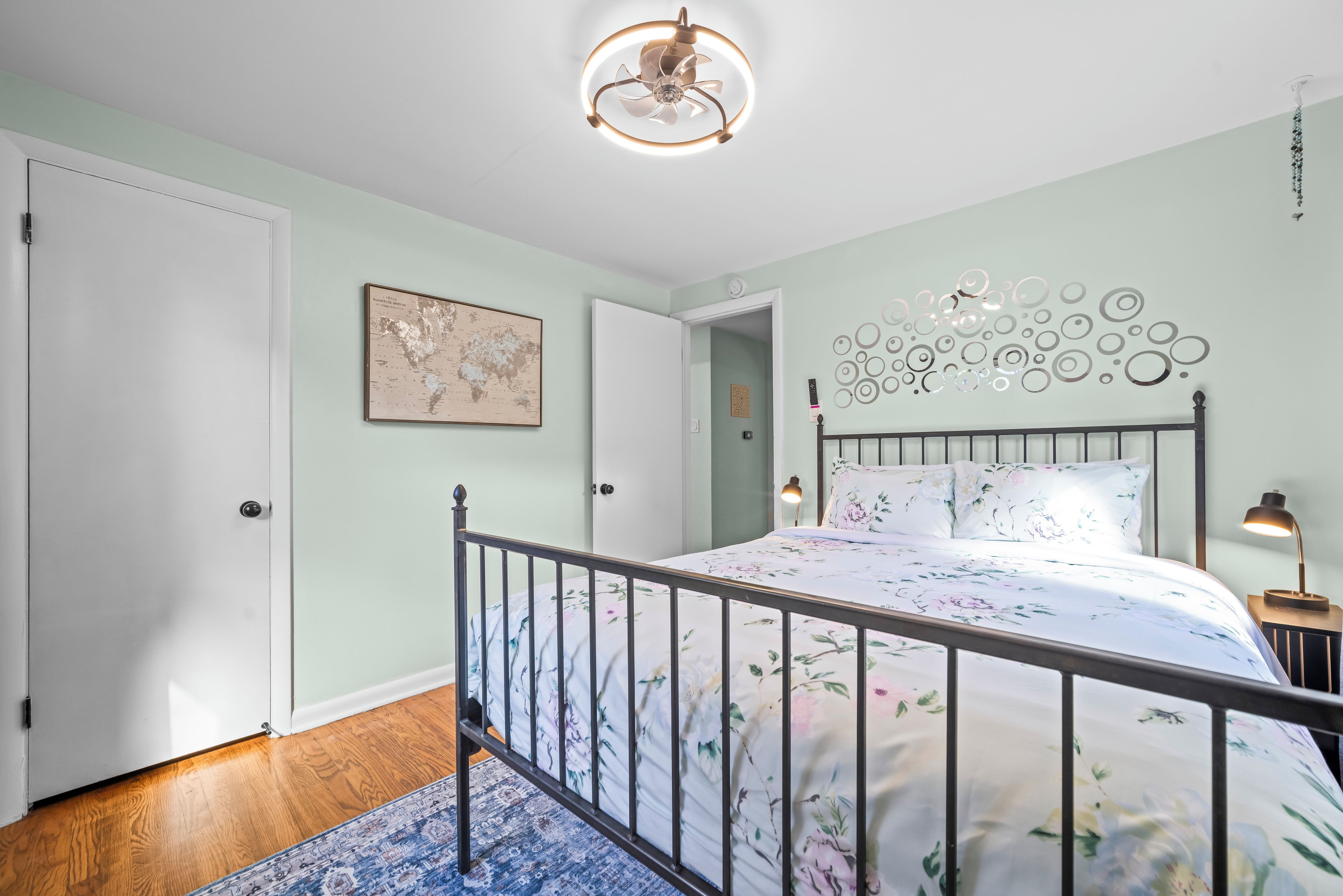 A bedroom with a bed, a world map on the wall, a decorative ceiling light, and a nightstand with a lamp.