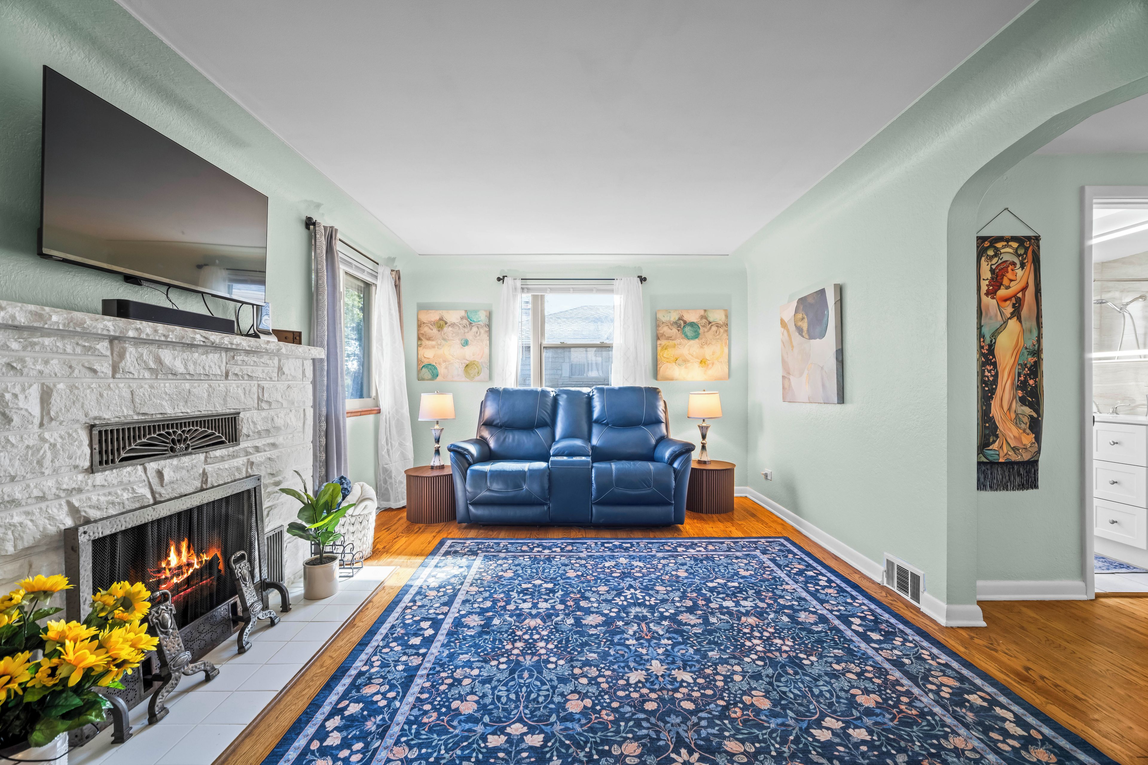 Een woonkamer met een open haard, een blauwe bank en een groot vloerkleed.
