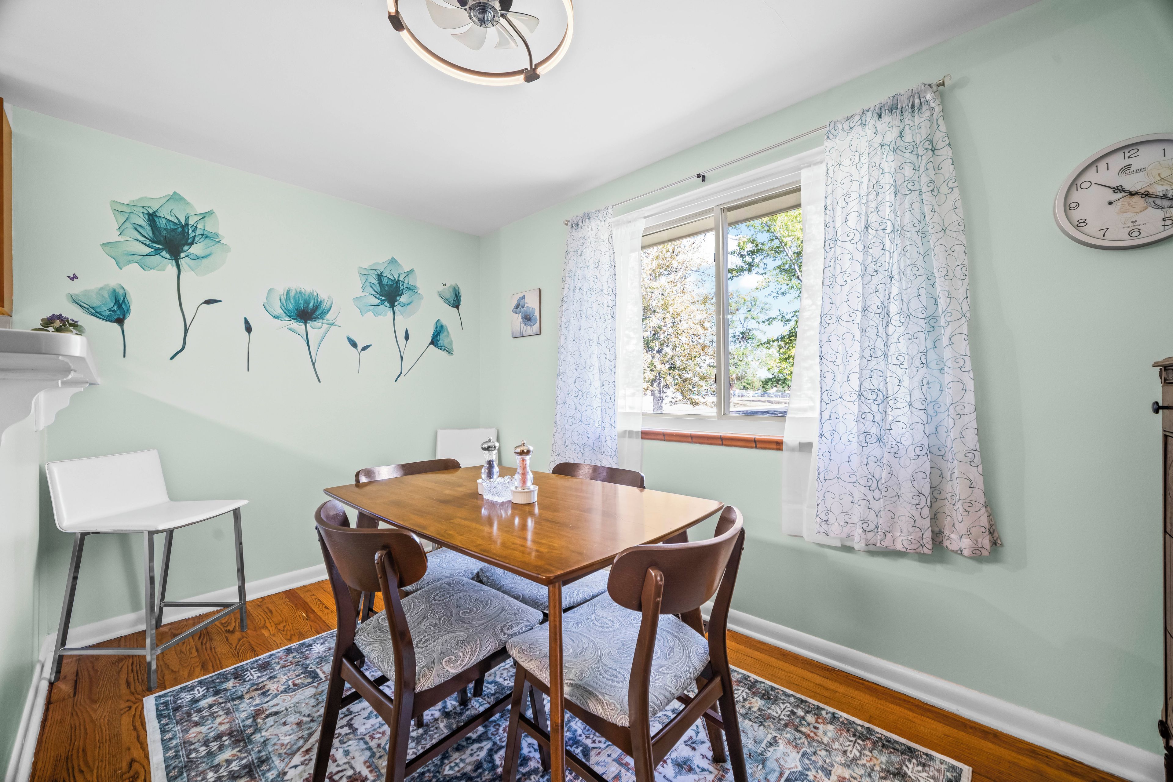 Comedor con mesa de madera, sillas, una lámpara de araña y una ventana con cortinas.
