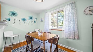 Comedor con mesa de madera, sillas, una lámpara de araña y una ventana con cortinas.