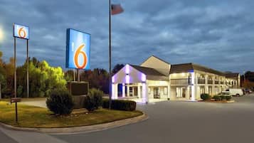 A motel with a large illuminated sign, a flag, and a well-lit building facade.