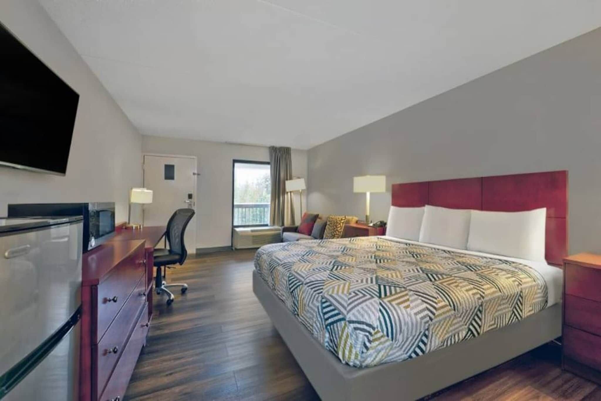A hotel room with a bed, desk, chair, and a TV.