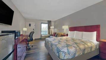 A hotel room with a bed, desk, chair, and a TV.
