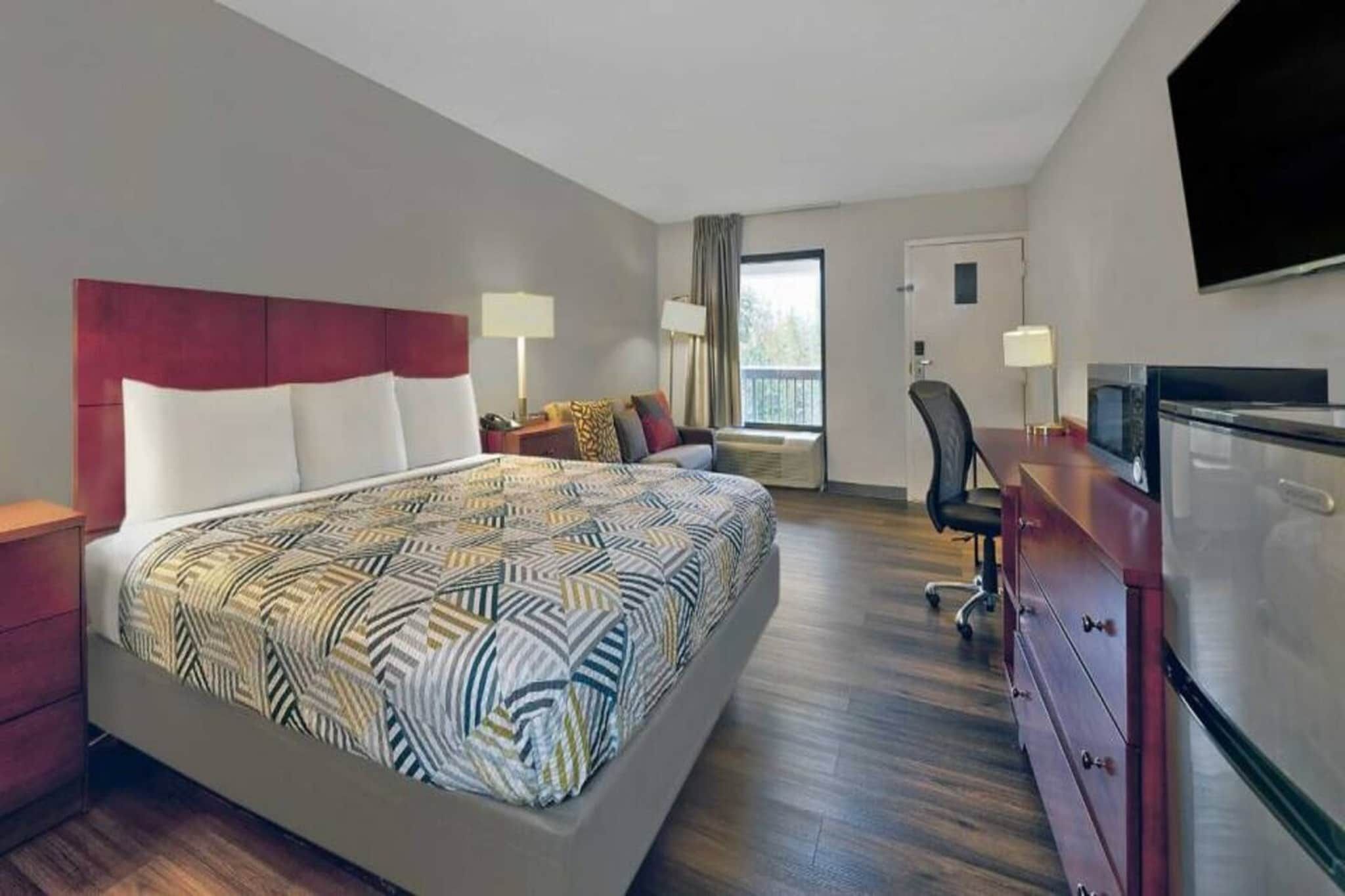 A hotel room with a large bed, a desk, a chair, a TV, and a wardrobe.