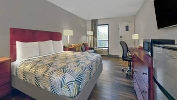 A hotel room with a large bed, a desk, a chair, a TV, and a wardrobe.