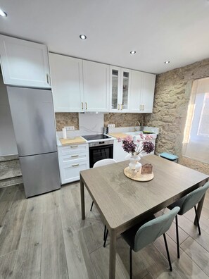 A modern kitchen with white cabinets, a stainless steel refrigerator, and a dining area with a wooden table and chairs. - ZOILA HOUSE (Queiruga- Porto do Son)