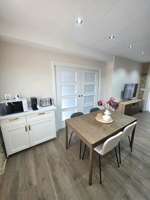 A modern kitchen with white cabinetry, a dining table with chairs, a coffee maker, a toaster, and a TV on a stand. - ZOILA HOUSE (Queiruga- Porto do Son)
