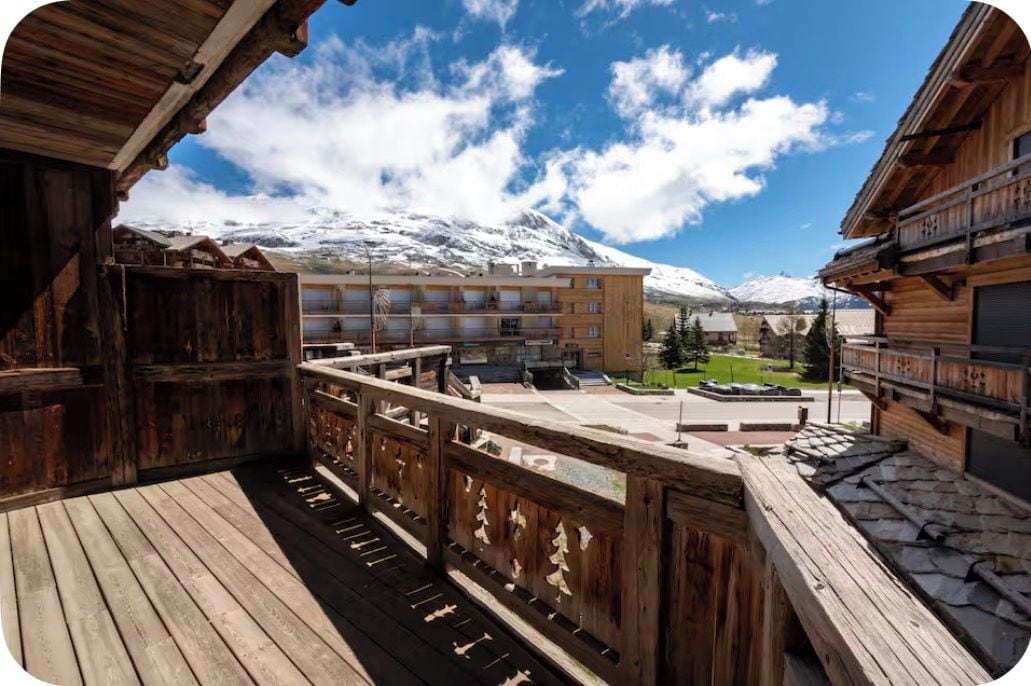 A wooden balcony with a view of a hotel building and snow-capped mountains.