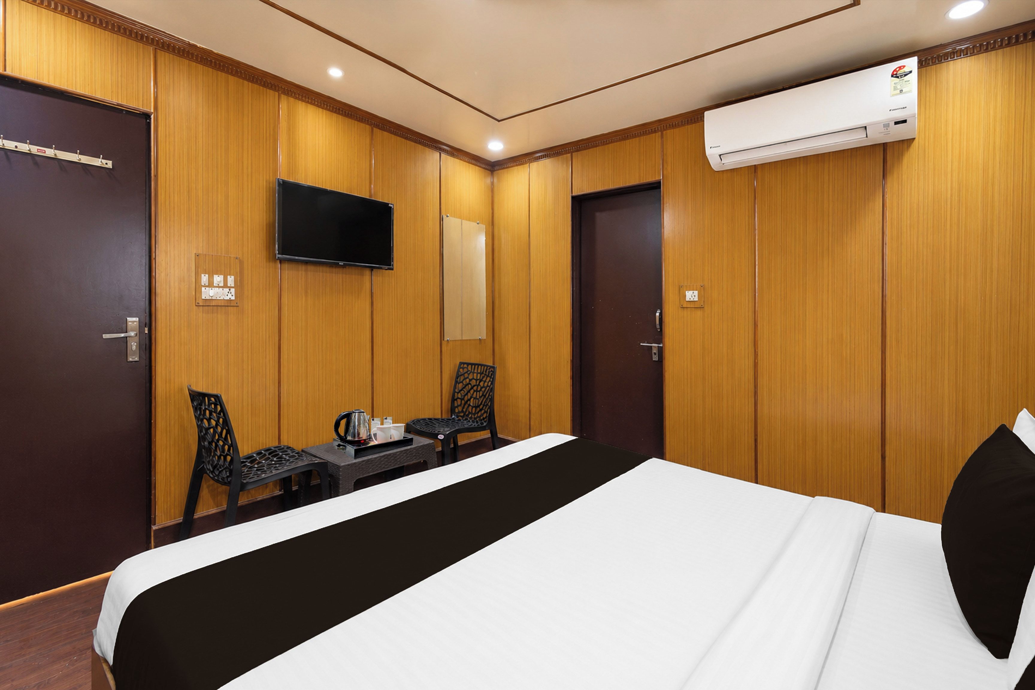 Ein Hotelzimmer mit einem Bett, einem Schreibtisch mit Stühlen, einem Fernseher und einer Klimaanlage.