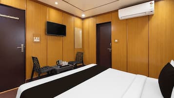 Ein Hotelzimmer mit einem Bett, einem Schreibtisch mit Stühlen, einem Fernseher und einer Klimaanlage.