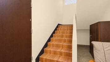 Una escalera de madera con peldaños que conducen a un rellano, una puerta de madera y un ventanal con un diseño de celosía.