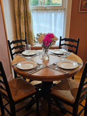 A round dining table with four chairs, a vase with flowers, and a window with curtains. - Charming, spacious apartment near to the beach. (Walmer)