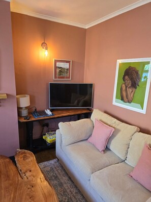 A living room with a beige sofa, a flat-screen TV, a chessboard, and a lamp. - Charming, spacious apartment near to the beach. (Walmer)