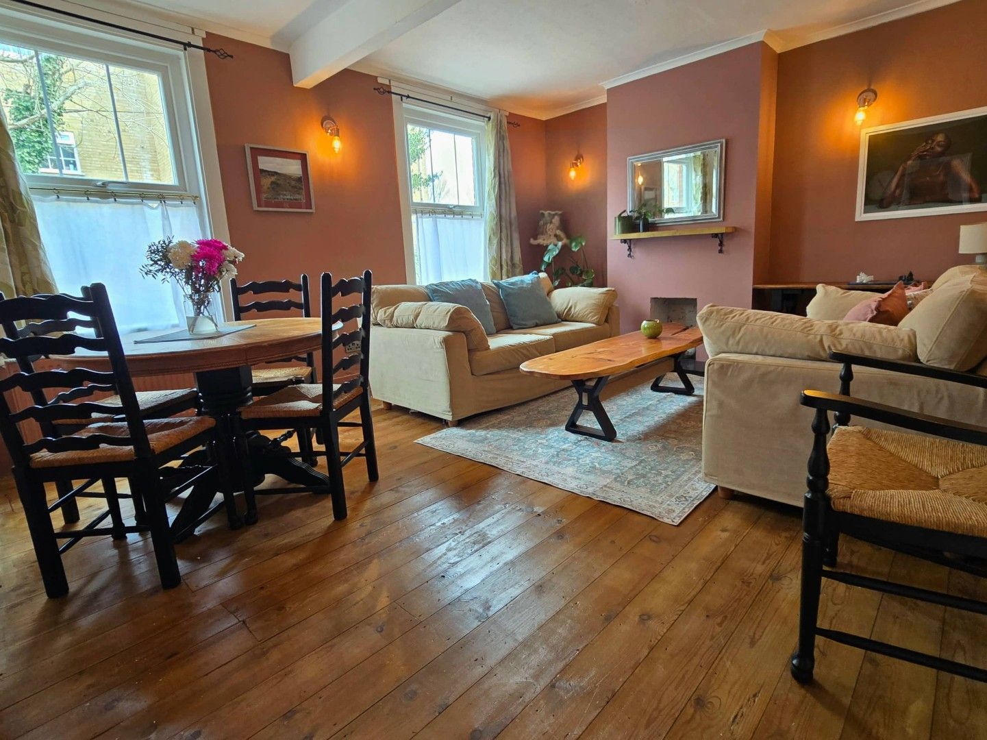 A living room with a wooden floor, a dining table with chairs, two sofas, a coffee table, and a fireplace.