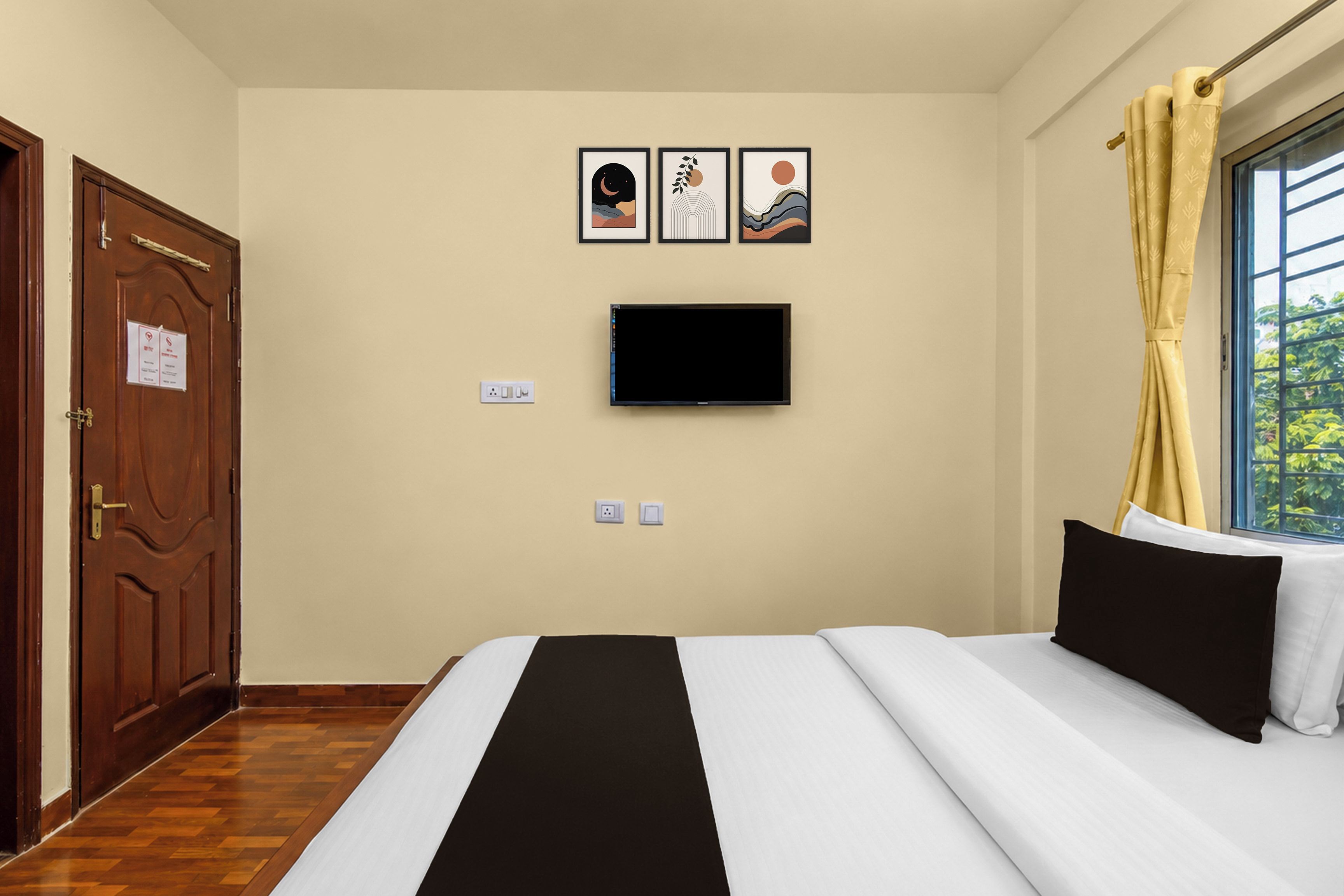 Habitación de hotel con cama, televisor montado en la pared y ventana con cortinas.