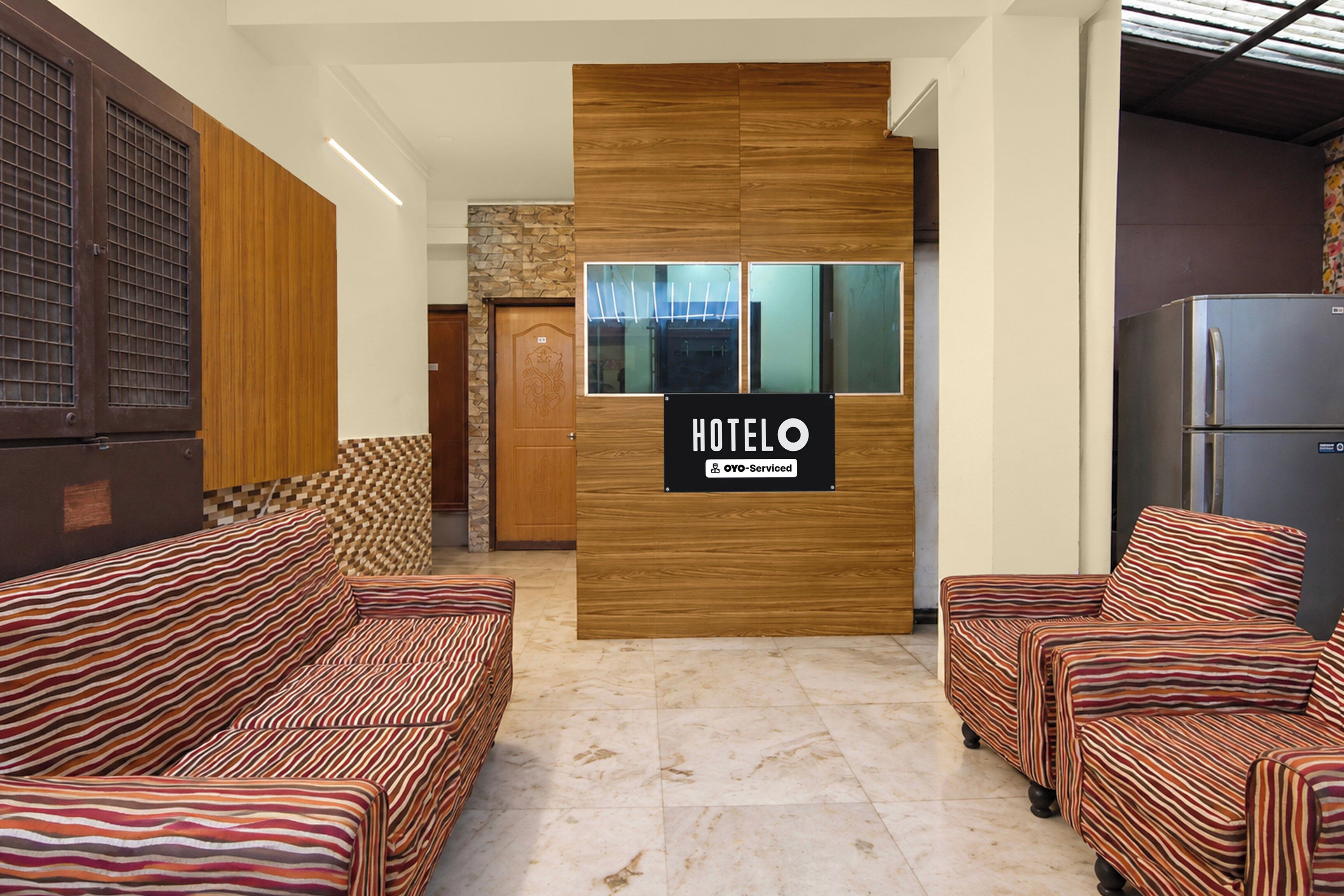 Zona de recepción de hotel con un mostrador de madera, un cartel que indica servicio de OYO y un refrigerador a la derecha.
