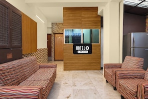 A hotel reception area with a wooden reception desk, a sign indicating it is serviced by OYO, and a refrigerator to the right. - Hotel O Biswa Bangla Gate  (Barasat)