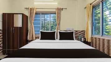 A hotel room with a bed, curtains, a wardrobe, a window, and a wall-mounted air conditioner.