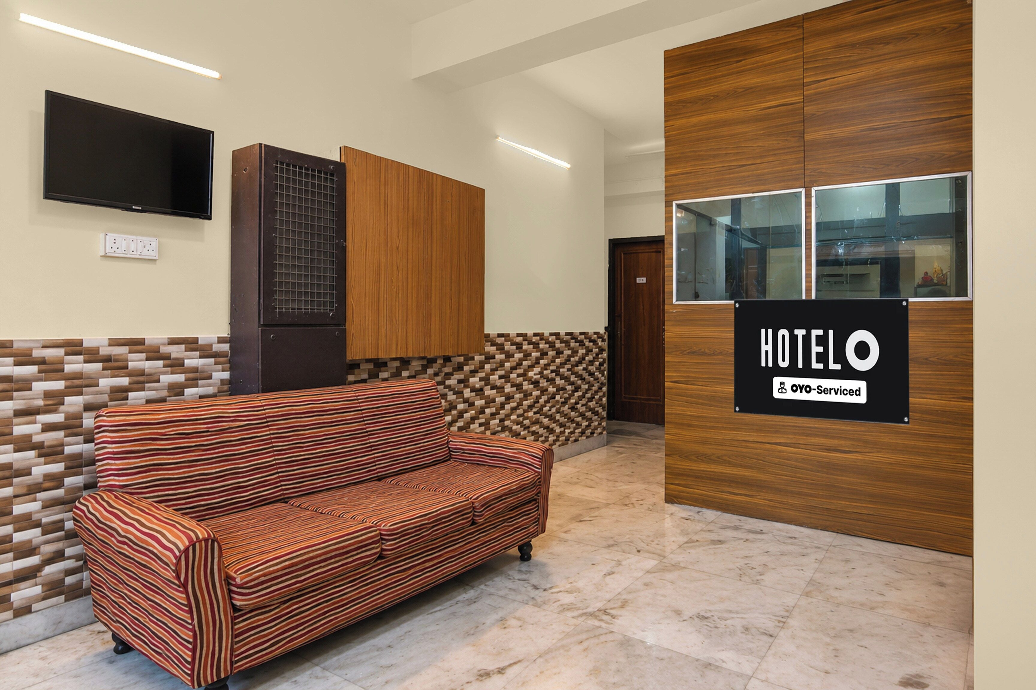 A hotel reception area with a sofa, a television, and a sign indicating the hotel name and OYO service.